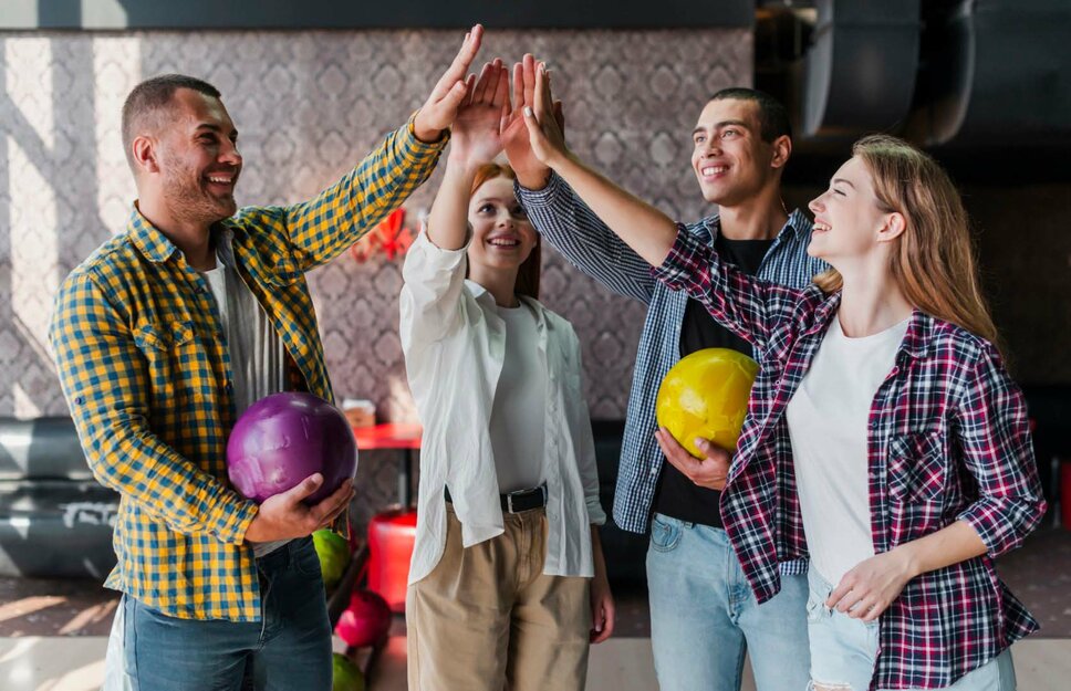  Eine Gruppe von vier jungen Menschen, die sich beim Bowling High-Fives geben, jeder hält eine Bowlingkugel in der Hand. Die Szene strahlt Freude, Teamgeist und Zusammenarbeit aus. Diese entspannte und freundliche Atmosphäre symbolisiert eine positive Arbeitskultur und Teamaktivitäten, wie sie bei Gatzsch Schweißtechnik gefördert werden. Die Personen wirken glücklich und motiviert, was auf ein starkes Gemeinschaftsgefühl und eine gute Work-Life-Balance im Unternehmen hinweist.