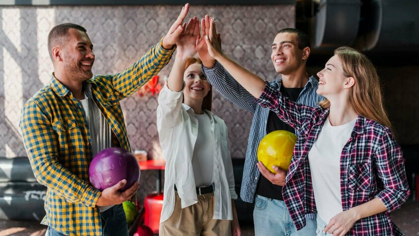  Eine Gruppe von vier jungen Menschen, die sich beim Bowling High-Fives geben, jeder hält eine Bowlingkugel in der Hand. Die Szene strahlt Freude, Teamgeist und Zusammenarbeit aus. Diese entspannte und freundliche Atmosphäre symbolisiert eine positive Arbeitskultur und Teamaktivitäten, wie sie bei Gatzsch Schweißtechnik gefördert werden. Die Personen wirken glücklich und motiviert, was auf ein starkes Gemeinschaftsgefühl und eine gute Work-Life-Balance im Unternehmen hinweist.