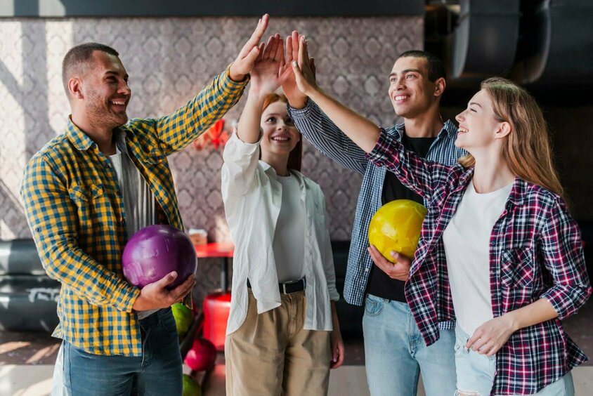  Eine Gruppe von vier jungen Menschen, die sich beim Bowling High-Fives geben, jeder hält eine Bowlingkugel in der Hand. Die Szene strahlt Freude, Teamgeist und Zusammenarbeit aus. Diese entspannte und freundliche Atmosphäre symbolisiert eine positive Arbeitskultur und Teamaktivitäten, wie sie bei Gatzsch Schweißtechnik gefördert werden. Die Personen wirken glücklich und motiviert, was auf ein starkes Gemeinschaftsgefühl und eine gute Work-Life-Balance im Unternehmen hinweist.