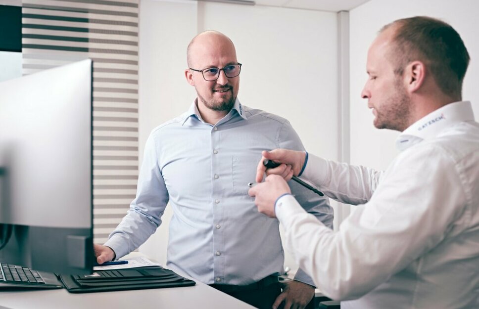 Zwei Männer in einem modernen Büro diskutieren vor einem Computerbildschirm technische Details. Beide tragen Hemden und wirken konzentriert auf die Aufgabe, während sie an einem Entwicklungsprojekt arbeiten. Die Szene symbolisiert Teamarbeit und technische Beratung, wie sie bei der Anlagenentwicklung bei Gatzsch Schweißtechnik stattfindet.