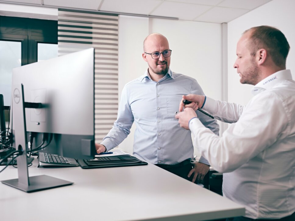 Zwei Männer in einem modernen Büro diskutieren vor einem Computerbildschirm technische Details. Beide tragen Hemden und wirken konzentriert auf die Aufgabe, während sie an einem Entwicklungsprojekt arbeiten. Die Szene symbolisiert Teamarbeit und technische Beratung, wie sie bei der Anlagenentwicklung bei Gatzsch Schweißtechnik stattfindet.