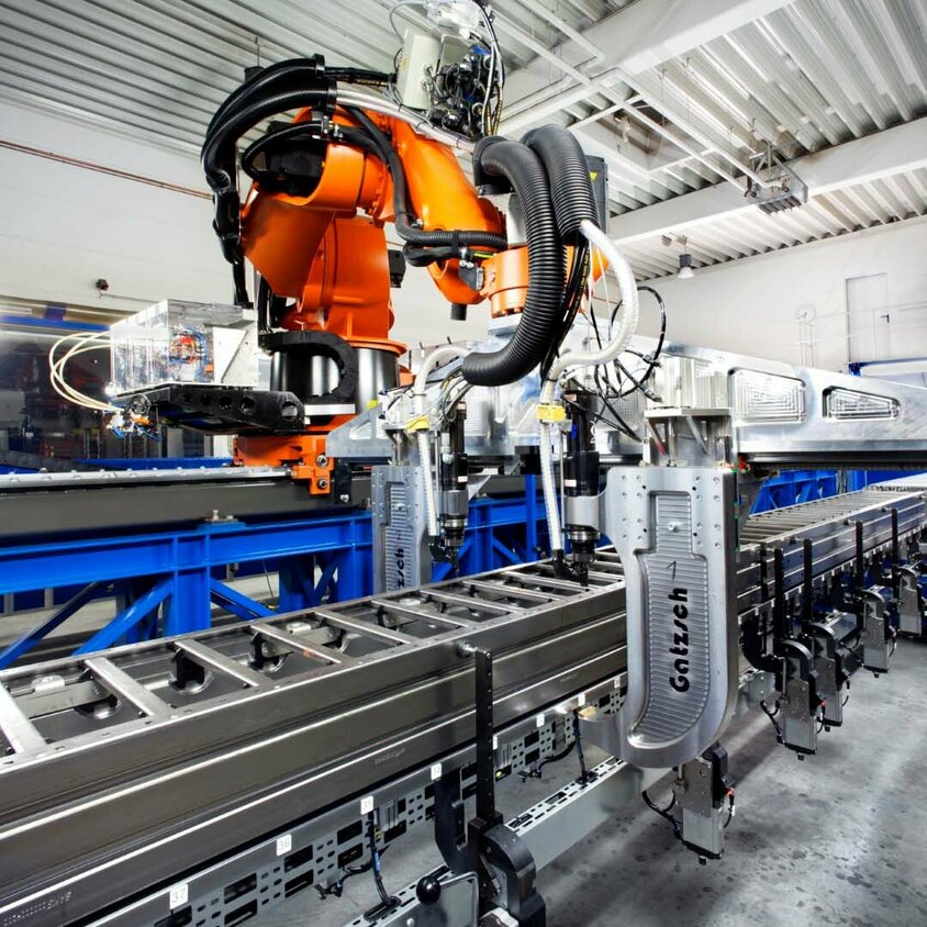 Ein moderner Industrieroboter in einer Produktionshalle, der an einer automatisierten Fertigungslinie arbeitet. Der Roboter führt Nieten und Clinchen durch, um Metallkomponenten präzise miteinander zu verbinden. Die Maschine, von der Firma Gatzsch Schweißtechnik,  ist an einer Förderanlage befestigt und befindet sich in einer hellen, industriellen Umgebung.