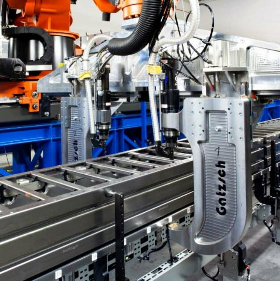 Ein moderner Industrieroboter in einer Produktionshalle, der an einer automatisierten Fertigungslinie arbeitet. Der Roboter führt Nieten und Clinchen durch, um Metallkomponenten präzise miteinander zu verbinden. Die Maschine, von der Firma Gatzsch Schweißtechnik,  ist an einer Förderanlage befestigt und befindet sich in einer hellen, industriellen Umgebung.