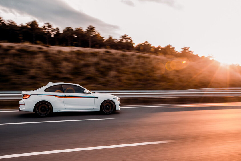 Ein weißes Auto fährt dynamisch auf einer Autobahn bei Sonnenuntergang, was symbolisch für die Automobilindustrie steht. Diese Branche wird von Gatzsch Schweißtechnik mit Buckelschweißanlagen beliefert, die zur Herstellung robuster Verbindungen in Fahrzeugkomponenten verwendet werden. Das Bild unterstreicht die Bedeutung präziser Schweißtechnologie in der modernen Fahrzeugproduktion.