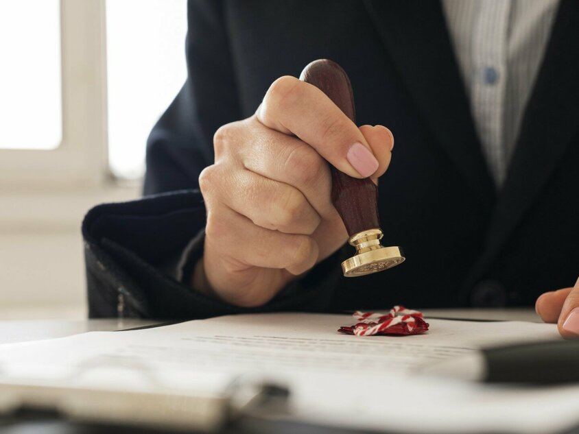 Eine Hand hält einen Siegelstempel und drückt diesen auf ein Dokument. Das Bild symbolisiert die Patente von Gatzsch Schweißtechnik im Bereich Warmnieten für die Verbindung zweier Metallbauteile.