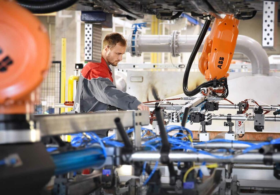 Ein Techniker von weba arbeitet an einer hochmodernen Produktionsanlage mit Robotik-Elementen. Der mobile Werkzeugbau-Service sorgt für die präzise Installation und Einarbeitung von Umform- und Stanzwerkzeugen in die Produktionsumgebung.